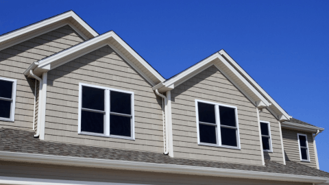 Completed tan siding job with gables and gutters against a blue sky