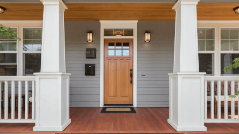 Front porch of a home with new gray-blue vinyl siding and a wood-tone entry door