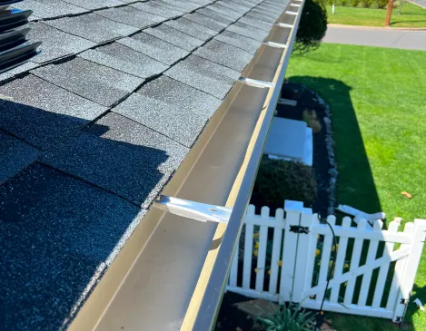 Finished gutter line along a shingle roof edge with a white picket fence below