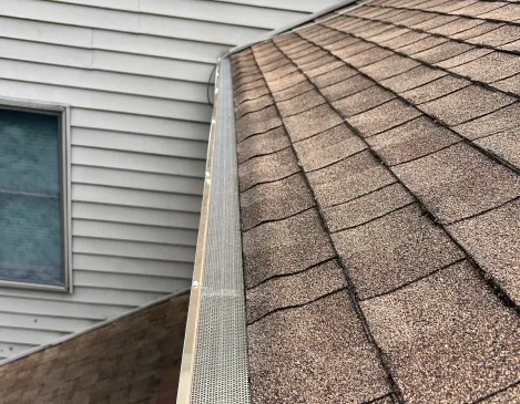 Gutter leaf guard installed against a shingle roof and siding