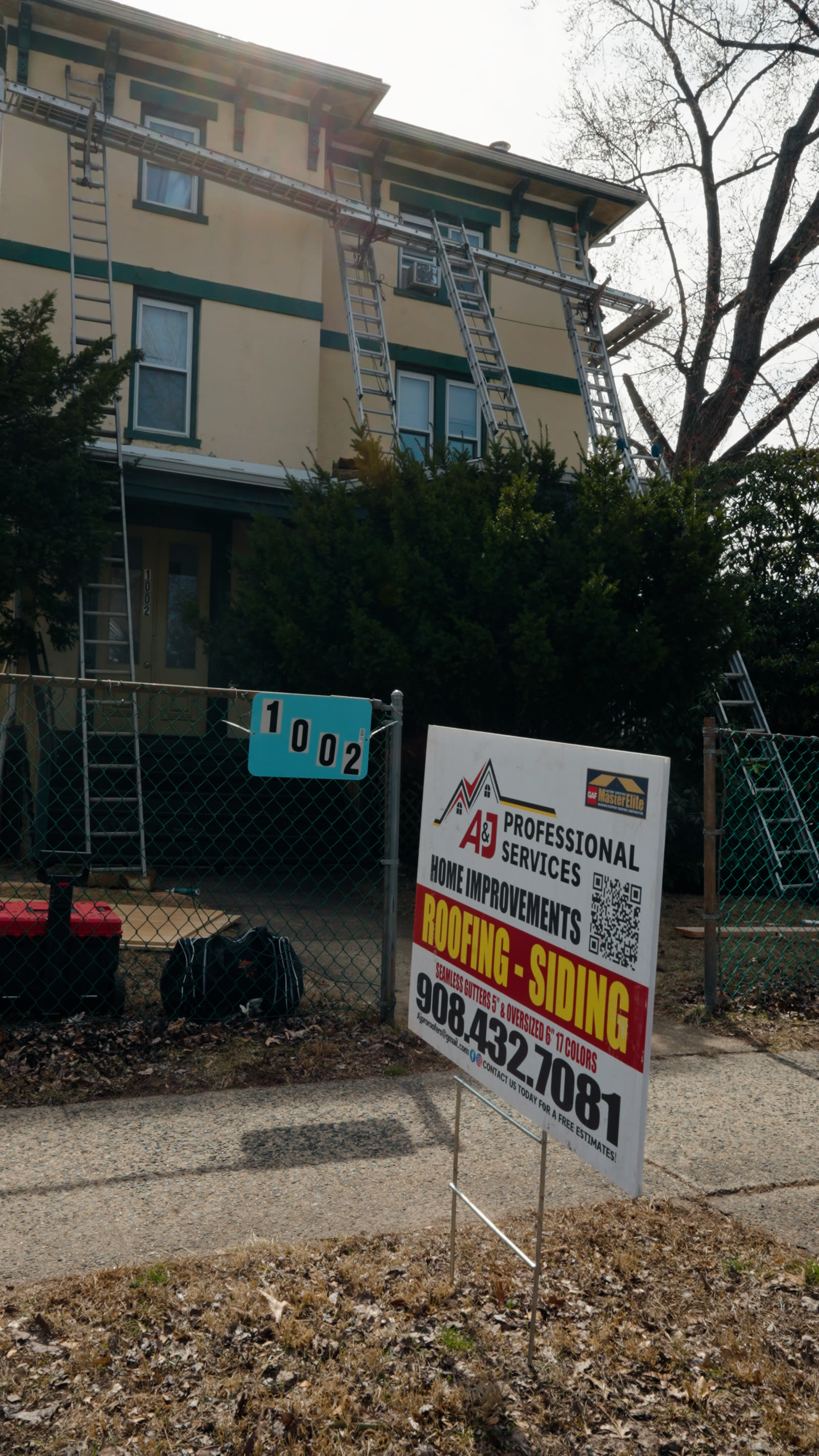 A&J job sign posted at a three-story multi-family building with ladders staged for an active job