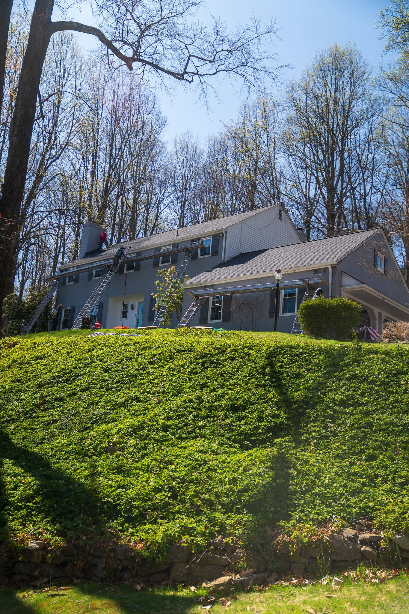 A&J crew on ladders at the roofline of a stone-and-siding two-story home during an active job
