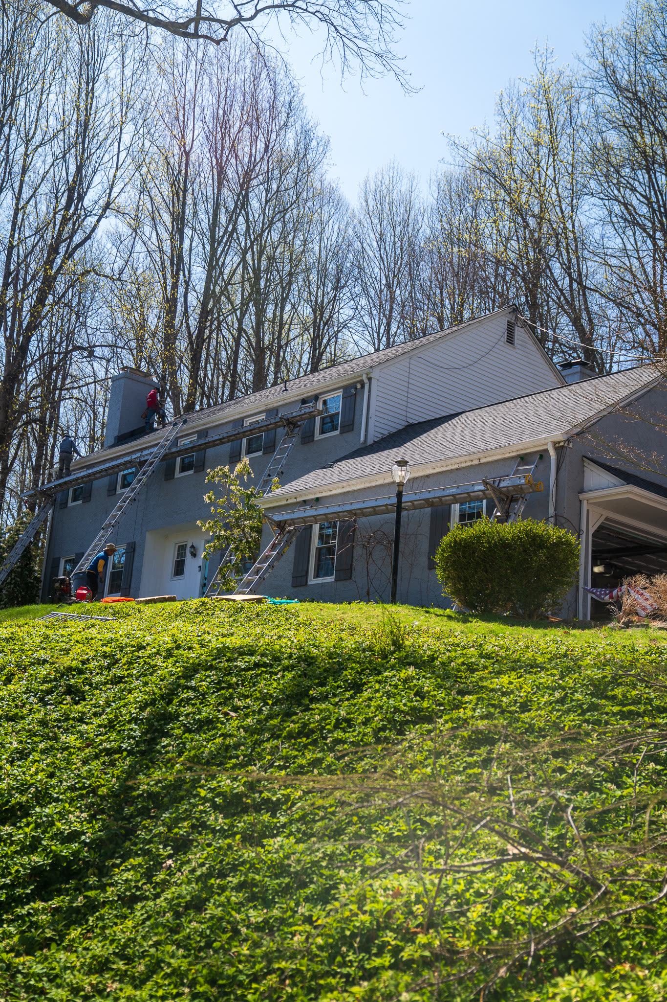 A&J crew on ladders at the roofline of a gray two-story colonial during an active job