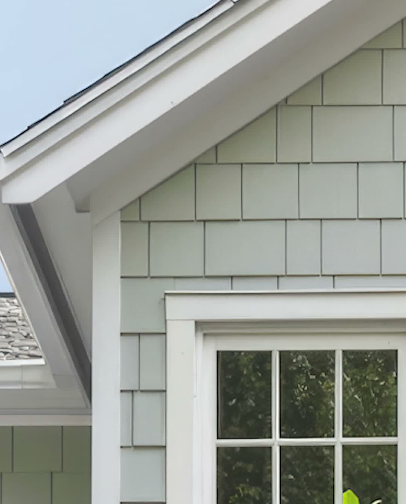 Finished light gray-green shake-style siding on a gable end, with white trim and window casing